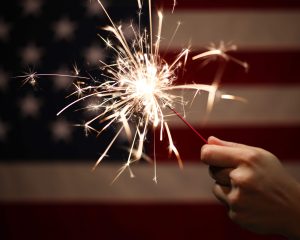 hand holding a sparkler in front of an american flag